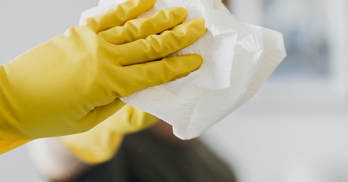 Anonymous male wearing yellow latex gloves and dark t shirt wiping mirror in bathroom with paper napkin