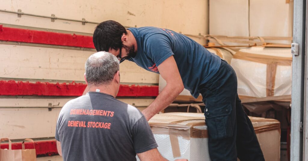 Faceless removal porters in uniform unloading big white boxes off lorry while working in delivery service